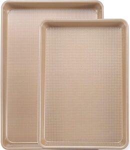 Two gold-colored rectangular baking sheets with textured surfaces, one larger and one smaller, are stacked with the smaller sheet slightly overlapping the larger one.