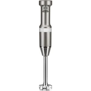 A metallic handheld immersion blender with a cylindrical handle, a power button near the top, and a detachable blending arm with a blade guard at the bottom. The brand name is visible on the handle.