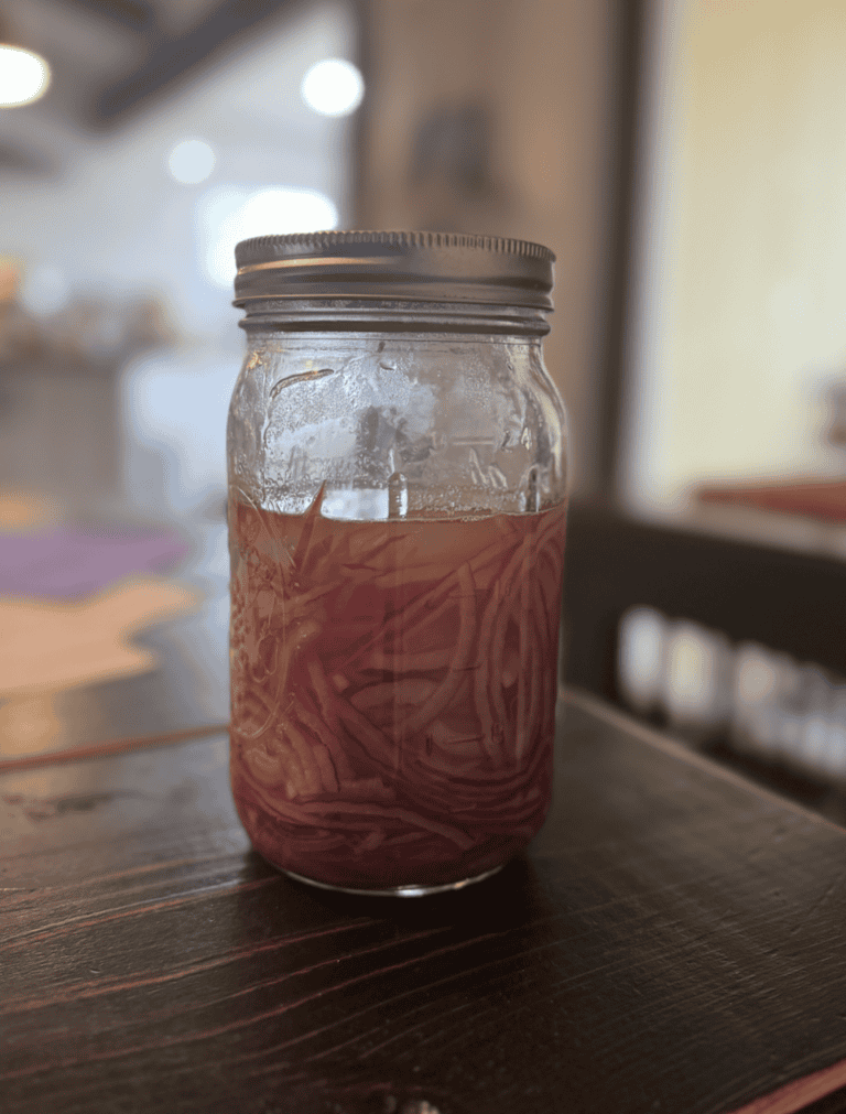 Honey Pickled Onions in a sealed mason jar on a brown table.