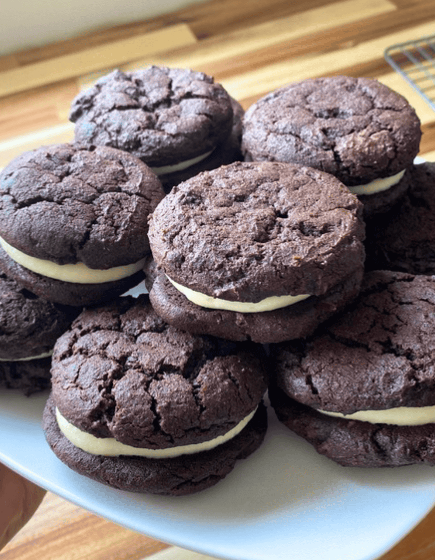 Two stacks of dark brown cookies with white cream in the middle on a white plate