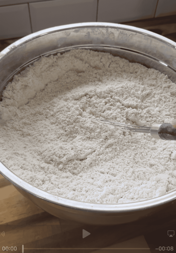 Flour in a large mixing bowl with a spoon, ready for baking or cooking.
