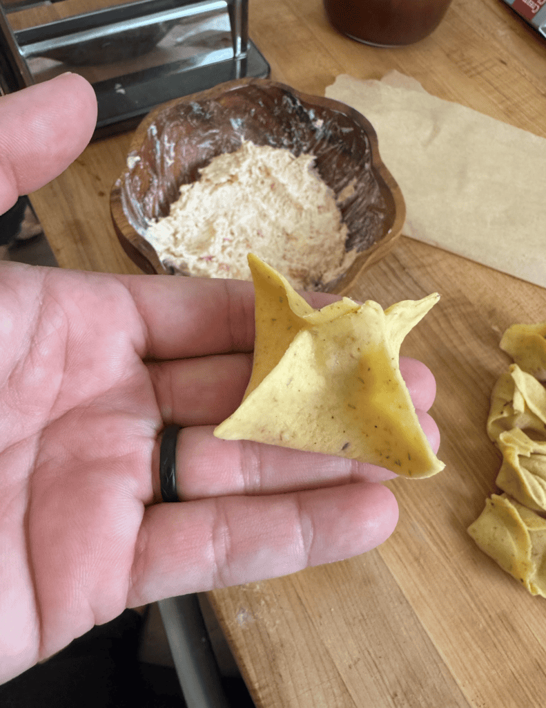 Crab rangoon formed with a bowl of crab rangoon filling in the background.