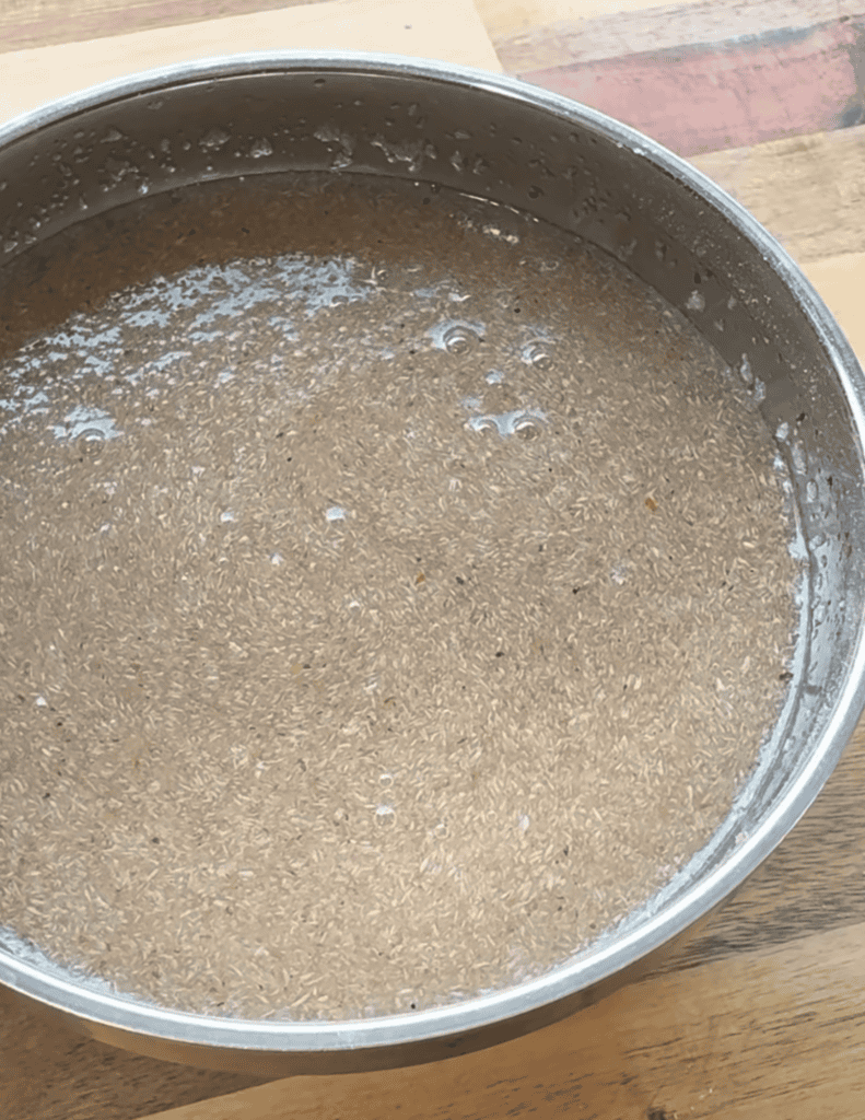 Soft, fluffy gluten-free pizza dough rising in a metal bowl on a wooden surface.