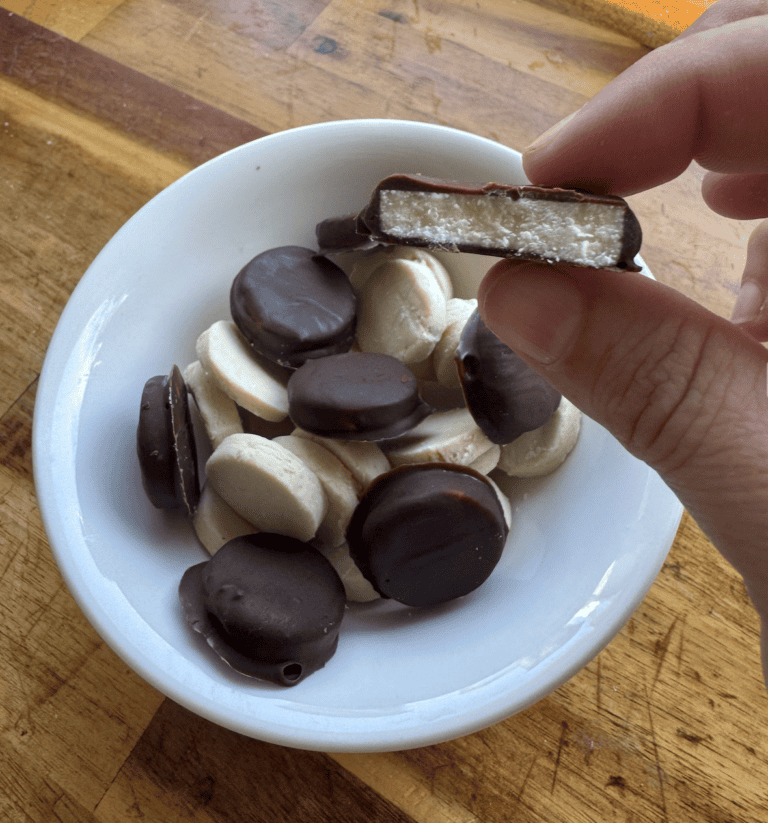 Bowl of peppermint patties, some covered in chocolate and some not. One half eaten peppermint patty in hand.