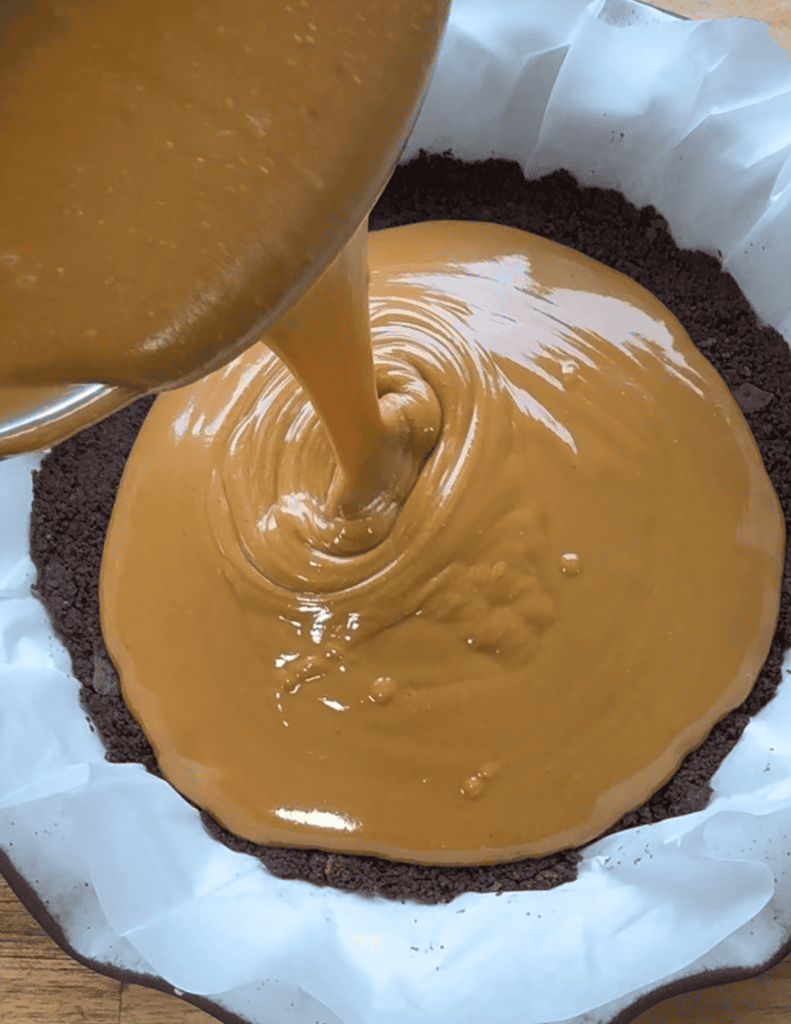Triple layer dessert cake peanut butter layer being poured into a chocolate cake base.