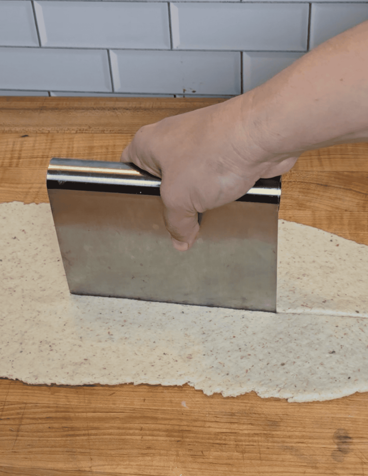 using a dough scraper to cut the dough in half so it can go through the roller