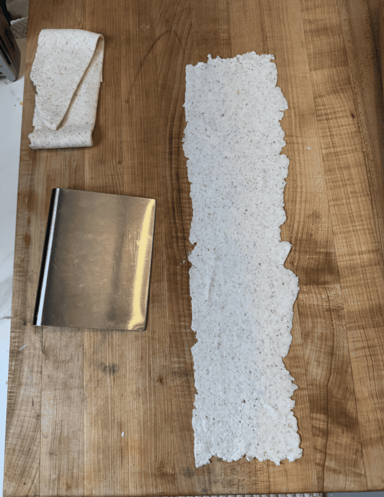 gluten free dumpling dough rolled thin with a dough scraper next to it preparing for it to get cut.