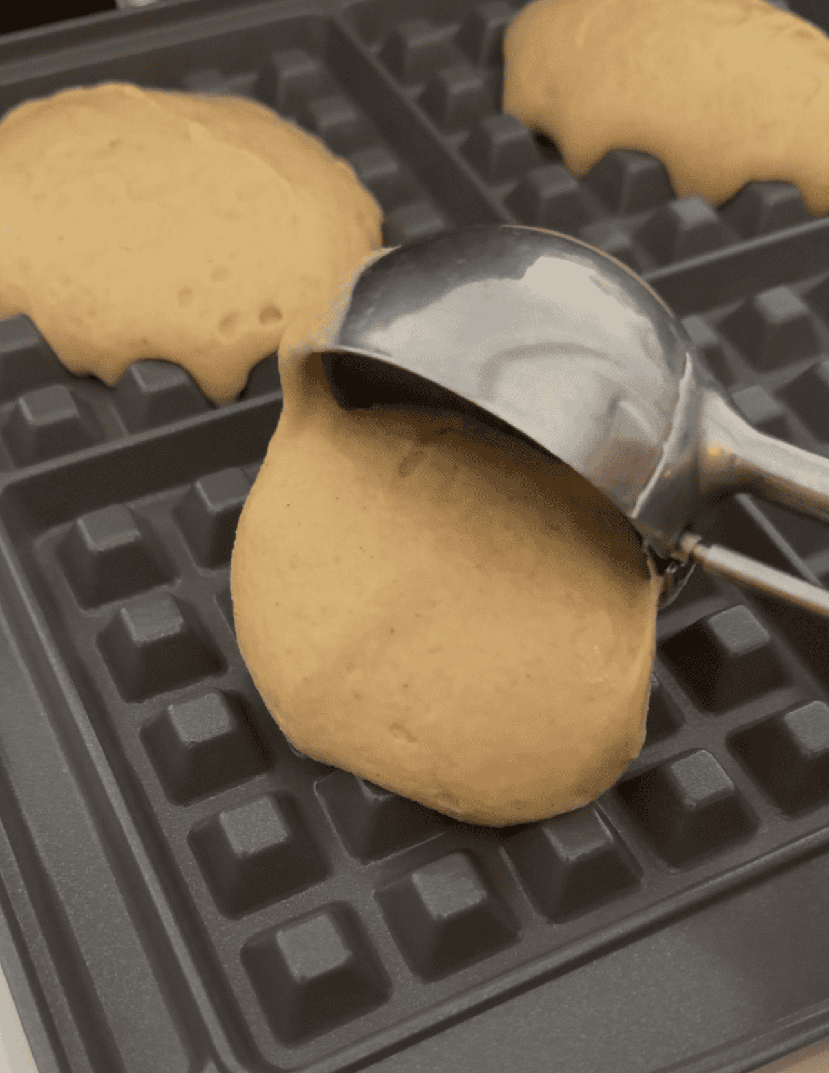 Gluten free waffle batter being scooped onto a waffle iron.