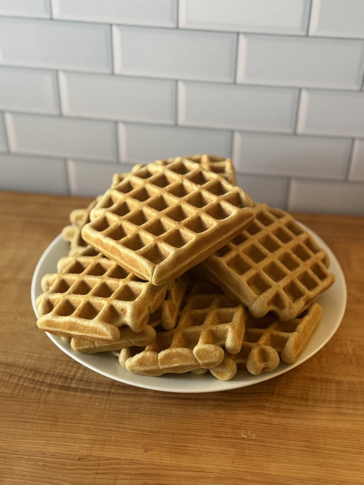 Gluten free waffles towered on top of each other on a white plate.