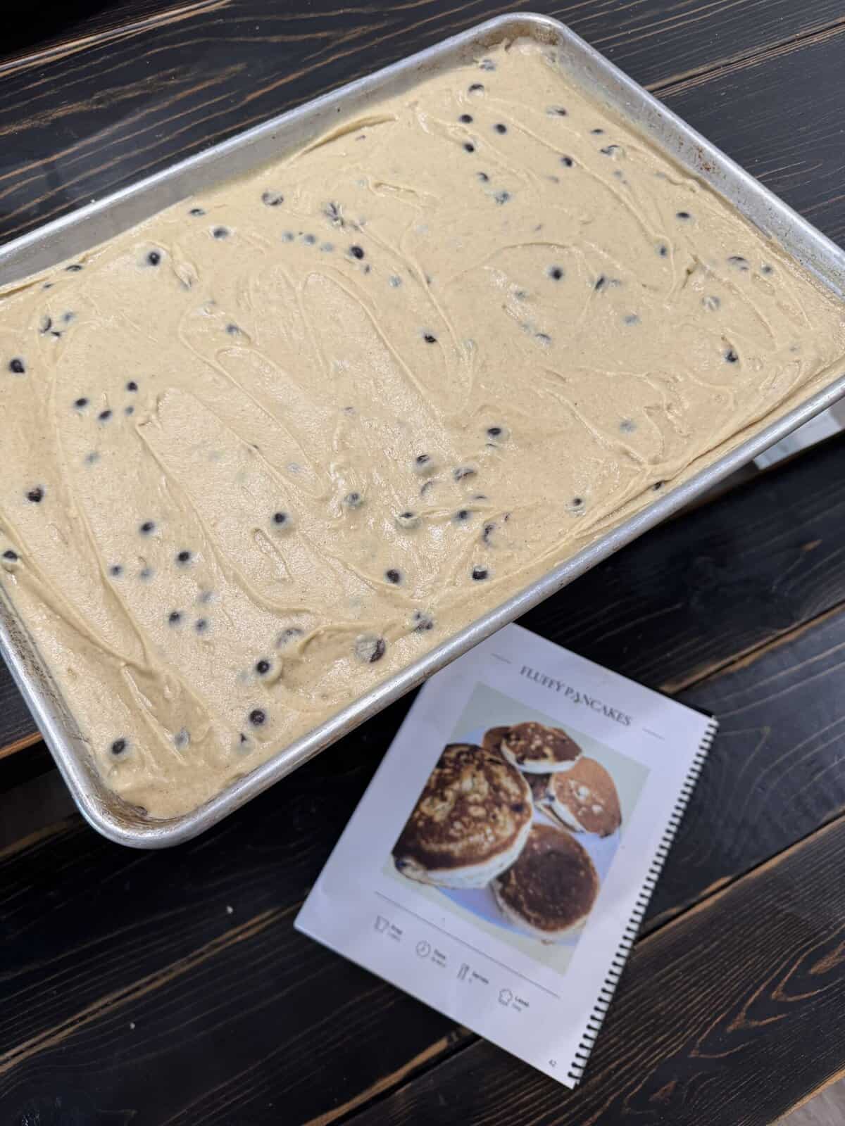 gluten free chocolate chip pancake batter spread out on a sheet pan with the cookbook page opened next to it.