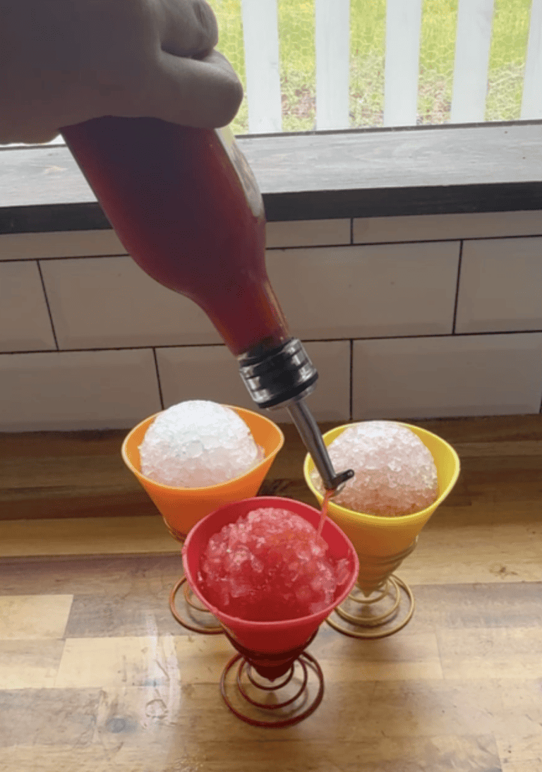 Strawberry Snow Cone Syrup pouring over top of a snow cone