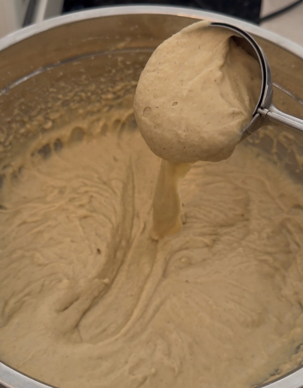 Gluten free waffle batter being scooped out of a stainless steel bowl with an ice cream scoop.