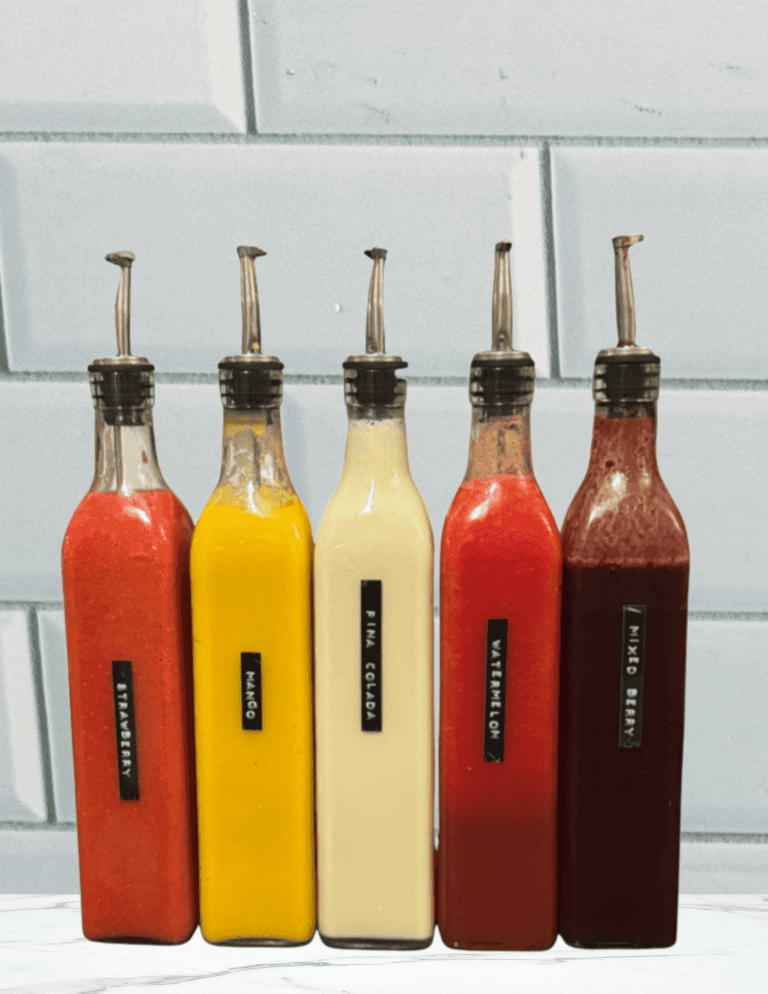 Five flavors of refined sugar free and dye free snow cone syrups in glass dispenser bottles.