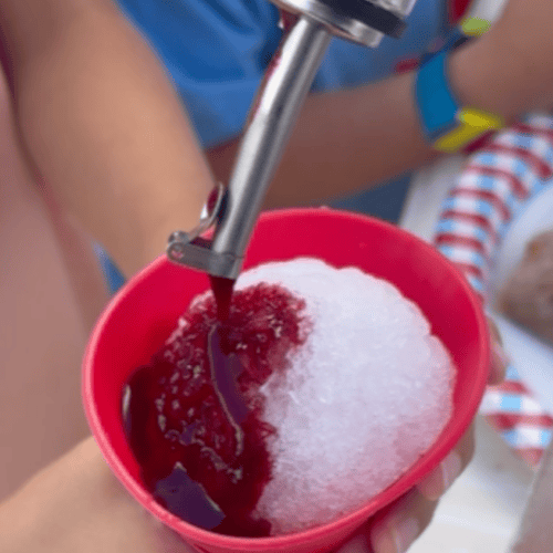 Dye-free and refined sugar free mixed berry snow cone syrup being poured over shaved ice in a red silicone cup.