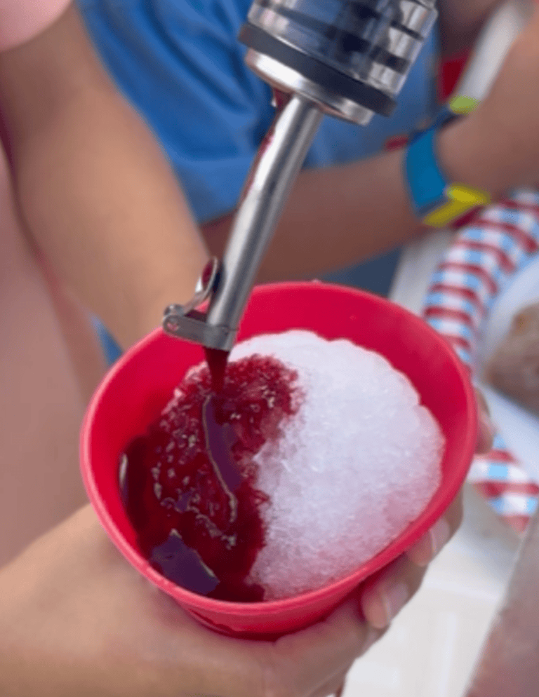 Dye-free and refined sugar free mixed berry snow cone syrup being poured over shaved ice in a red silicone cup.