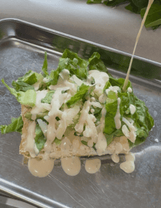 chicken caesar salad with chicken on the base, then lettuce, parmesan cheese, and caesar dressing.