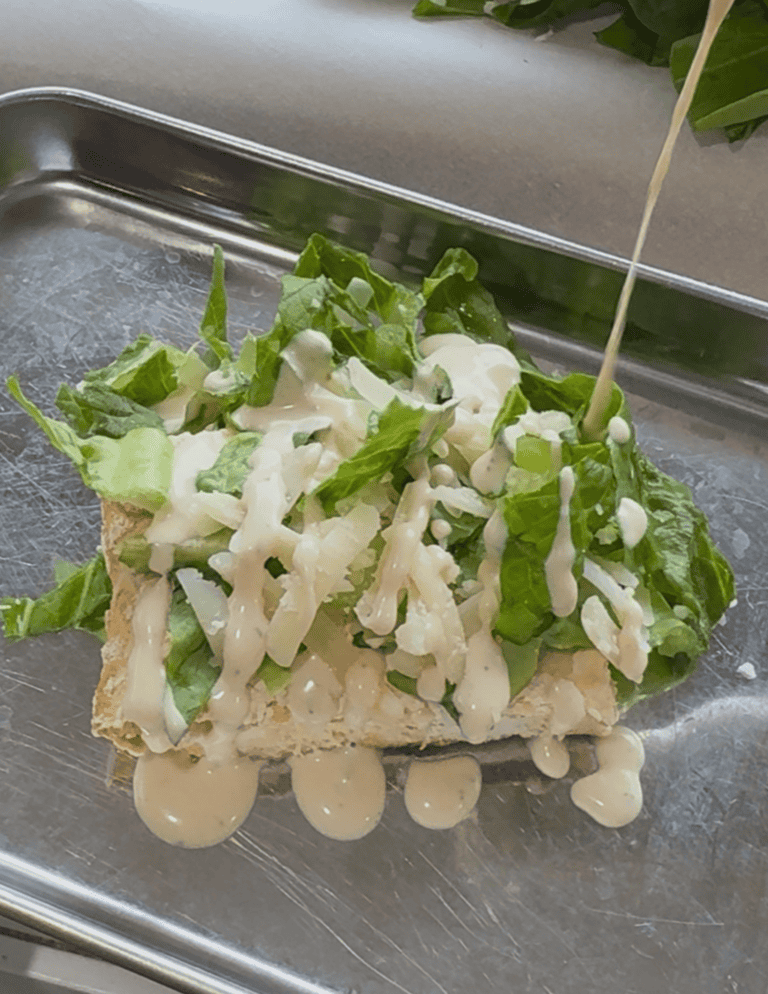 chicken caesar salad with chicken on the base, then lettuce, parmesan cheese, and caesar dressing.