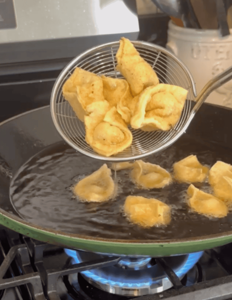 a spider strainer holding up fried wontons over the green wok.