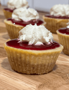 gluten free raspberry cheesecake bites with raspberry compote on top and whipped cream