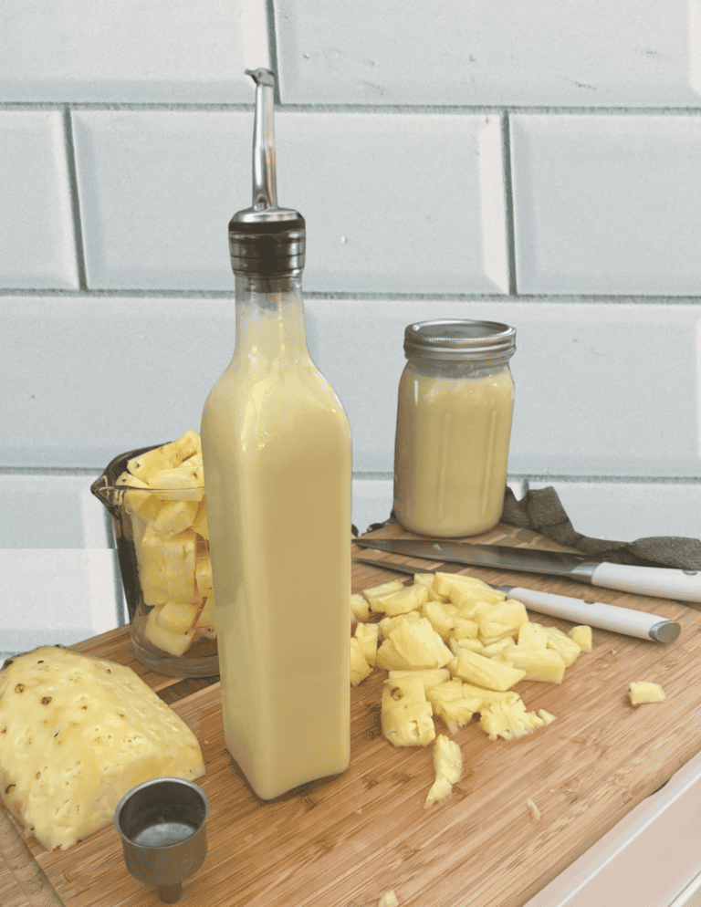 Pina colada snow cone syrup in a glass bottle with pineapple pieces cut up around it.