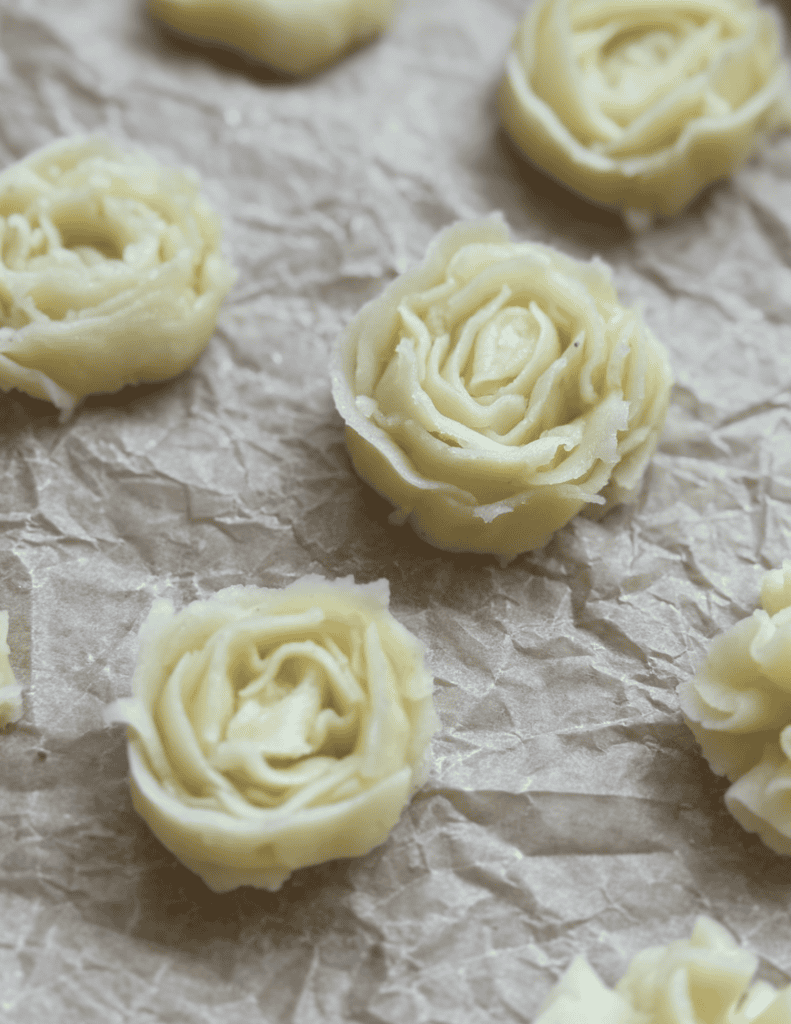 Butter cookies shaped like roses on parchment paper, showcasing fresh, homemade baked goods.