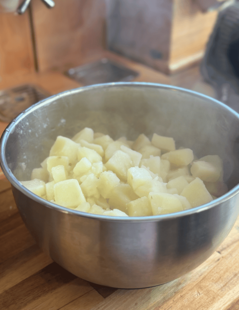 Mashed potatoes in a stainless steel bowl, steaming hot, ready to serve.