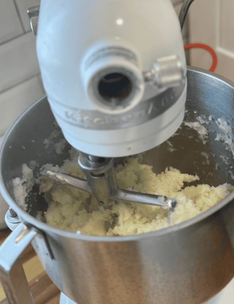 Stand mixer mixing mashed potatoes in a stainless steel bowl.