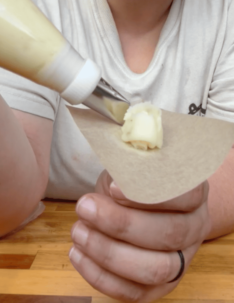 Person squeezing vanilla ice cream onto a cone with a piping bag.
