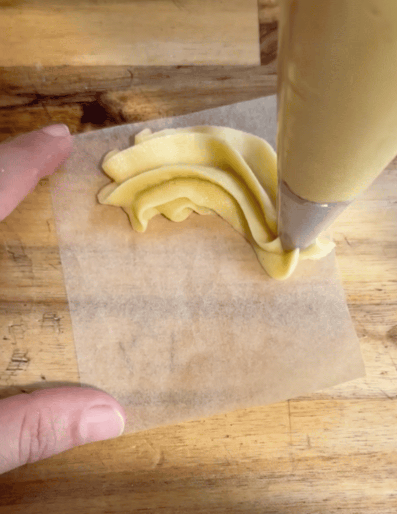 gluten free French cruller dough being pipped onto parchment paper to make a circle