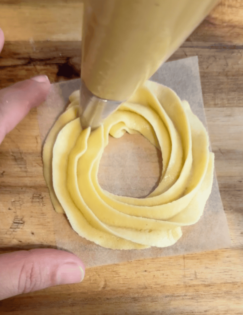 gluten free French cruller dough being pipped onto parchment paper to make a circle