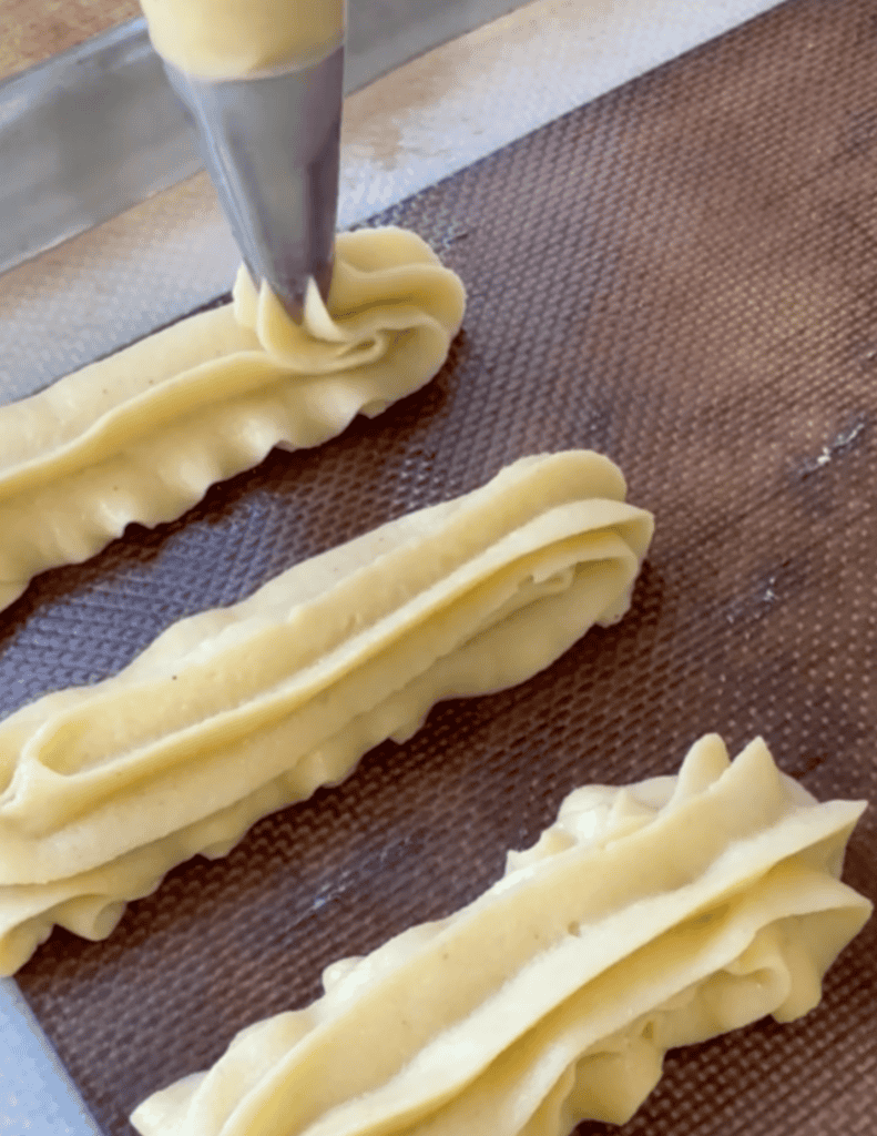 Fresh homemade pasta being piped onto a baking sheet for cooking.