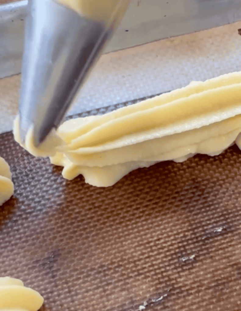 Eclair dough being piped onto a baking sheet for a fresh, farm-to-table meal.