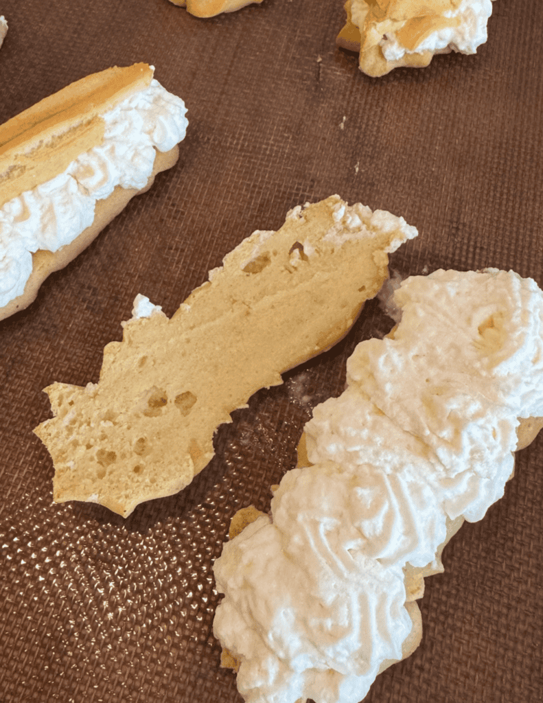 Ecalirs with fresh whipped cream on a baking sheet.