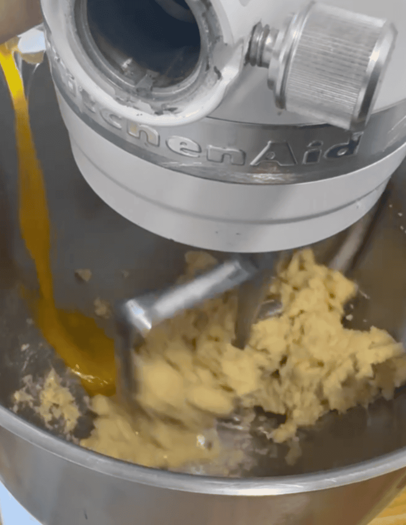 Commercial kitchen mixer blending dough with ingredients pouring in.