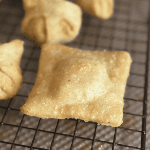 Fried pastry square on cooling rack with other baked treats in the background.