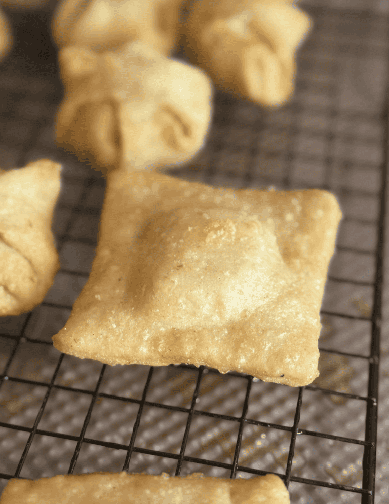Fried pastry square on cooling rack with other baked treats in the background.