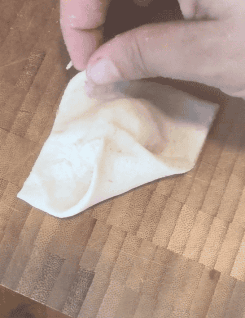 Hand making fresh dumpling wrappers on a wooden surface for homemade cooking.