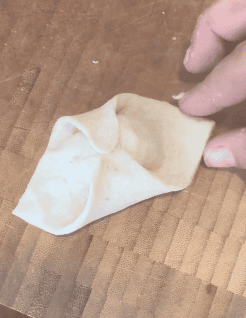 Hand holding a homemade dumpling wrapper on a wooden surface.