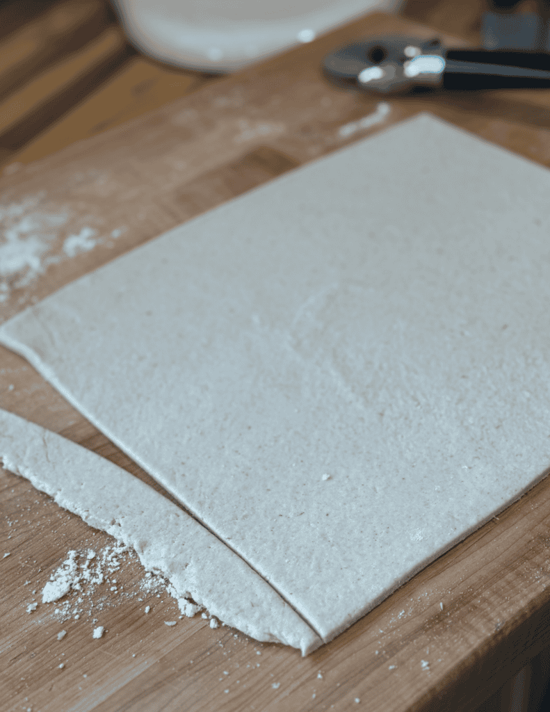 Fresh homemade dough sheet on a wooden surface with baking tools in the background.