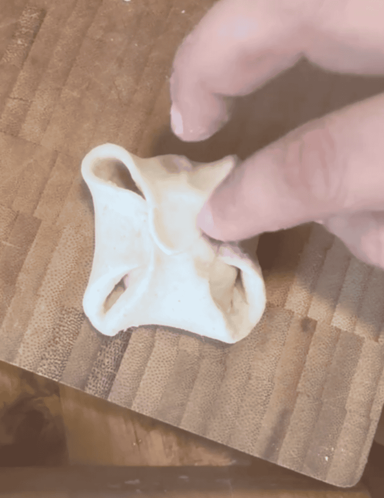 Hand pressing dough for homemade dumplings on a wooden surface.