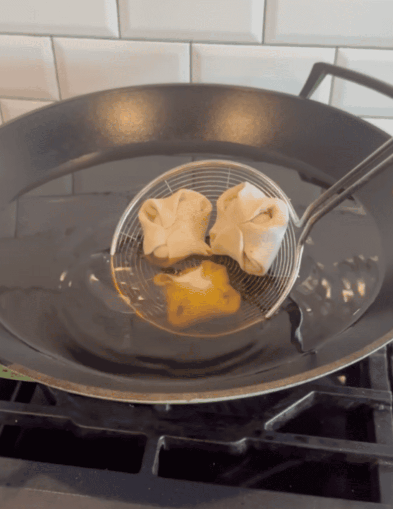 Frying dumplings in a black skillet with a slotted spoon, highlighting fresh, homemade food preparat.