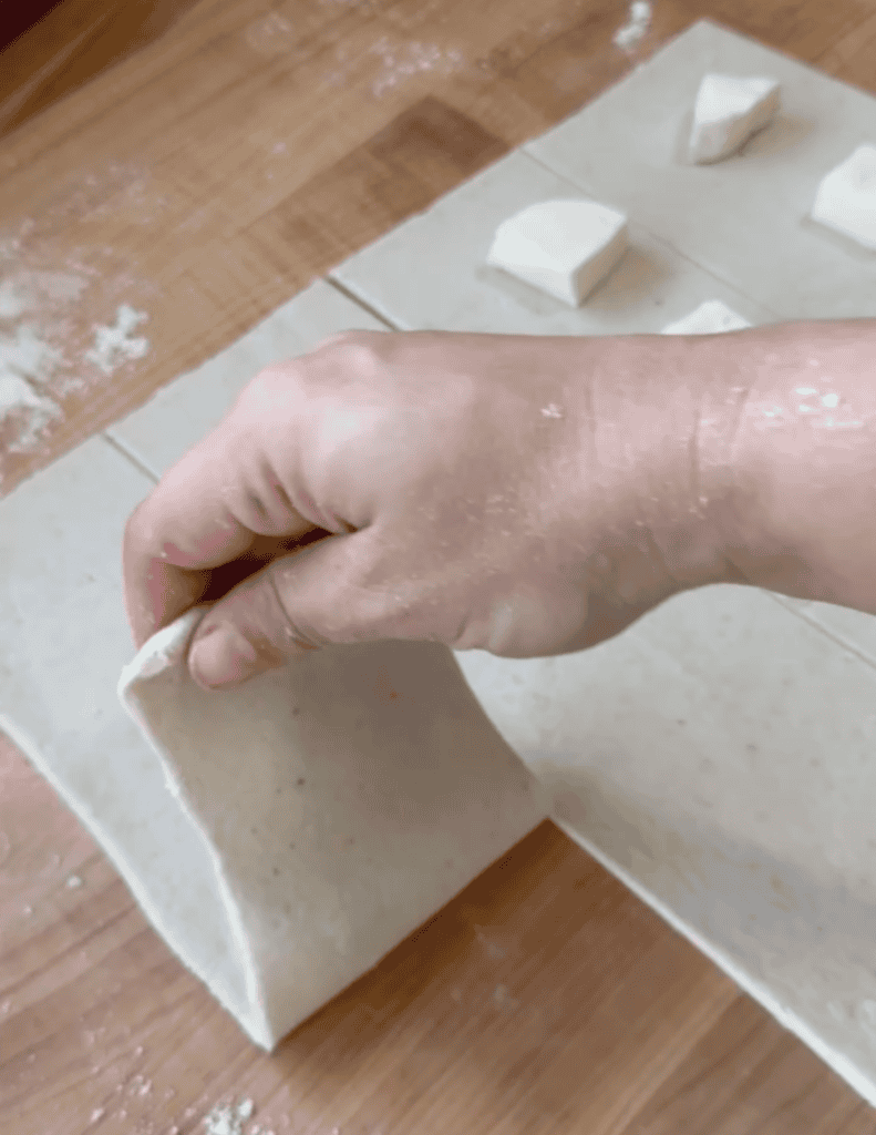 Hand shaping fresh cheese dough on parchment paper for homemade cheese.