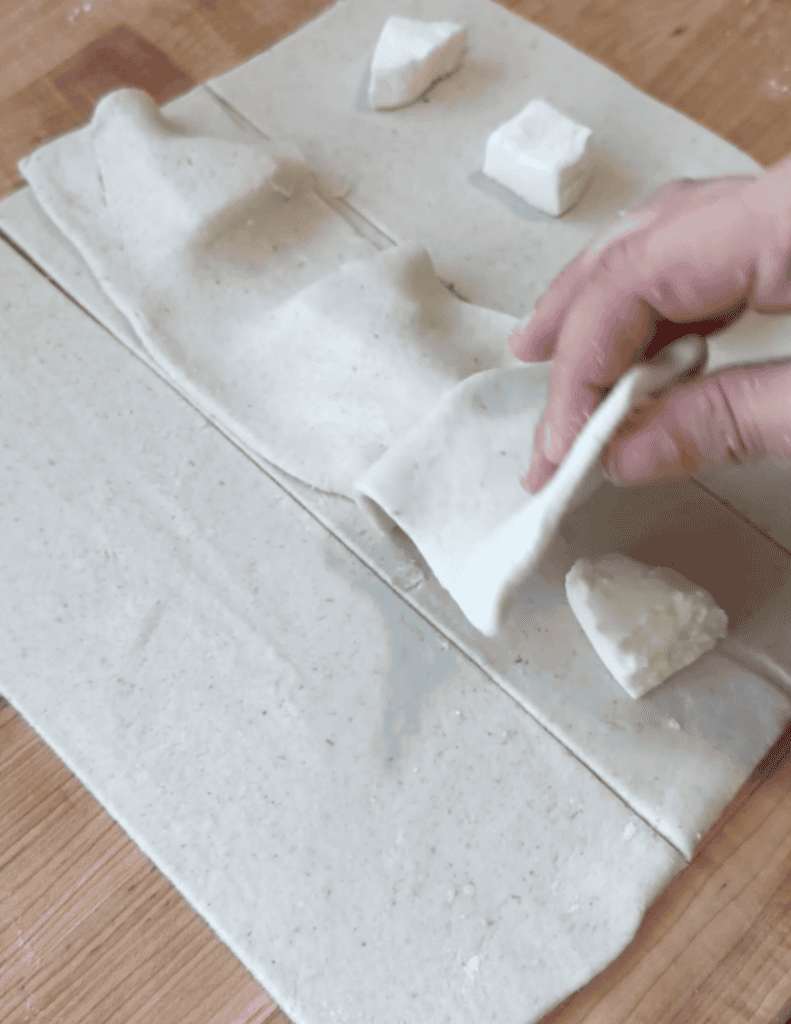 Hand rolling fresh cheese on parchment paper with butter cubes nearby.