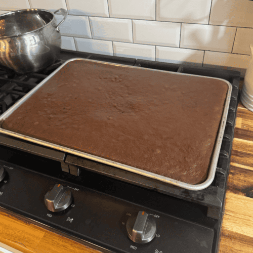 Freshly baked chocolate sheet cake cooling on a baking sheet in a cozy kitchen.