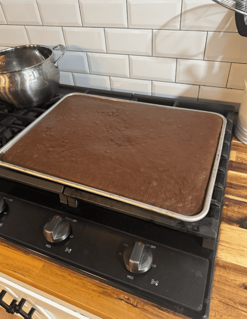Freshly baked chocolate sheet cake cooling on a baking sheet in a cozy kitchen.