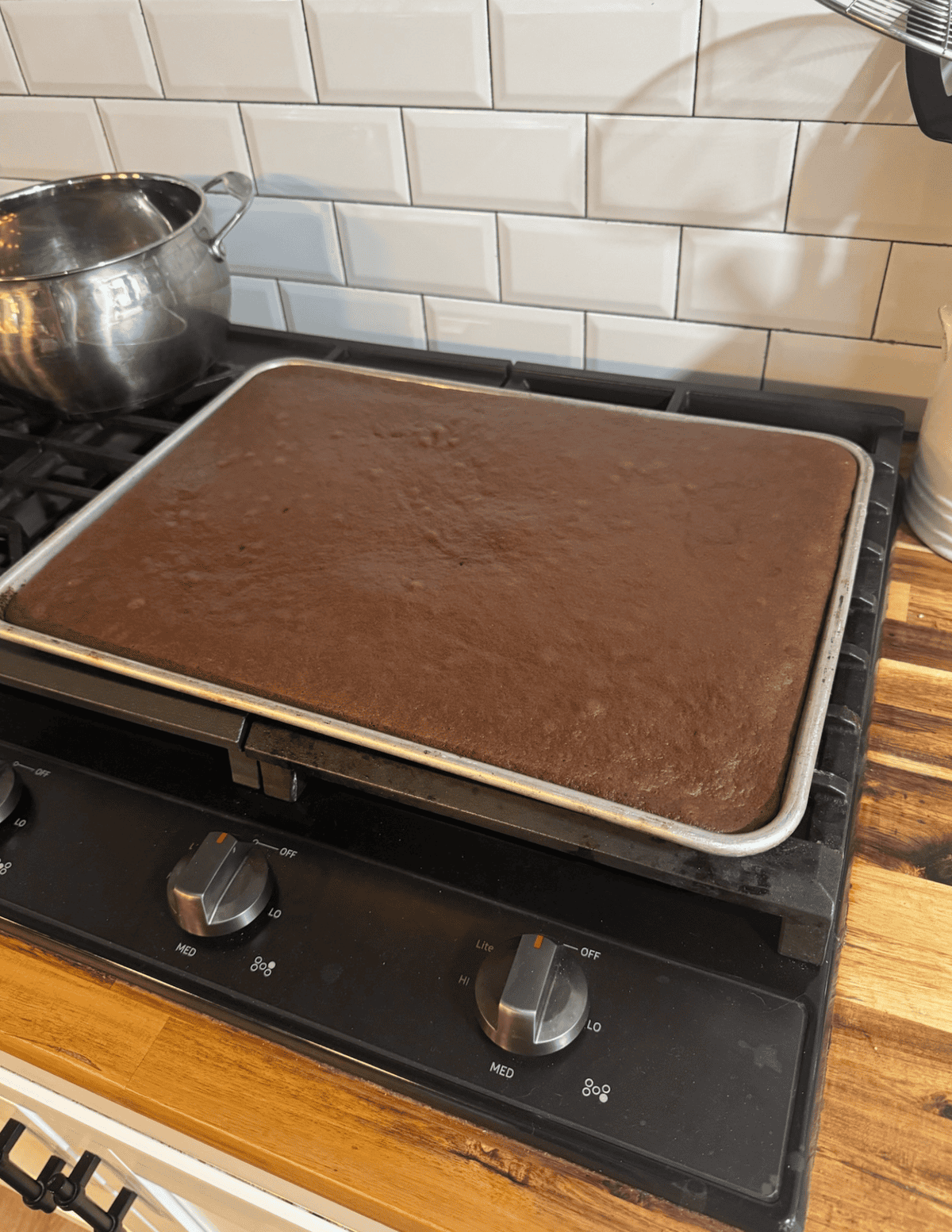 Freshly baked chocolate sheet cake cooling on a baking sheet in a cozy kitchen.