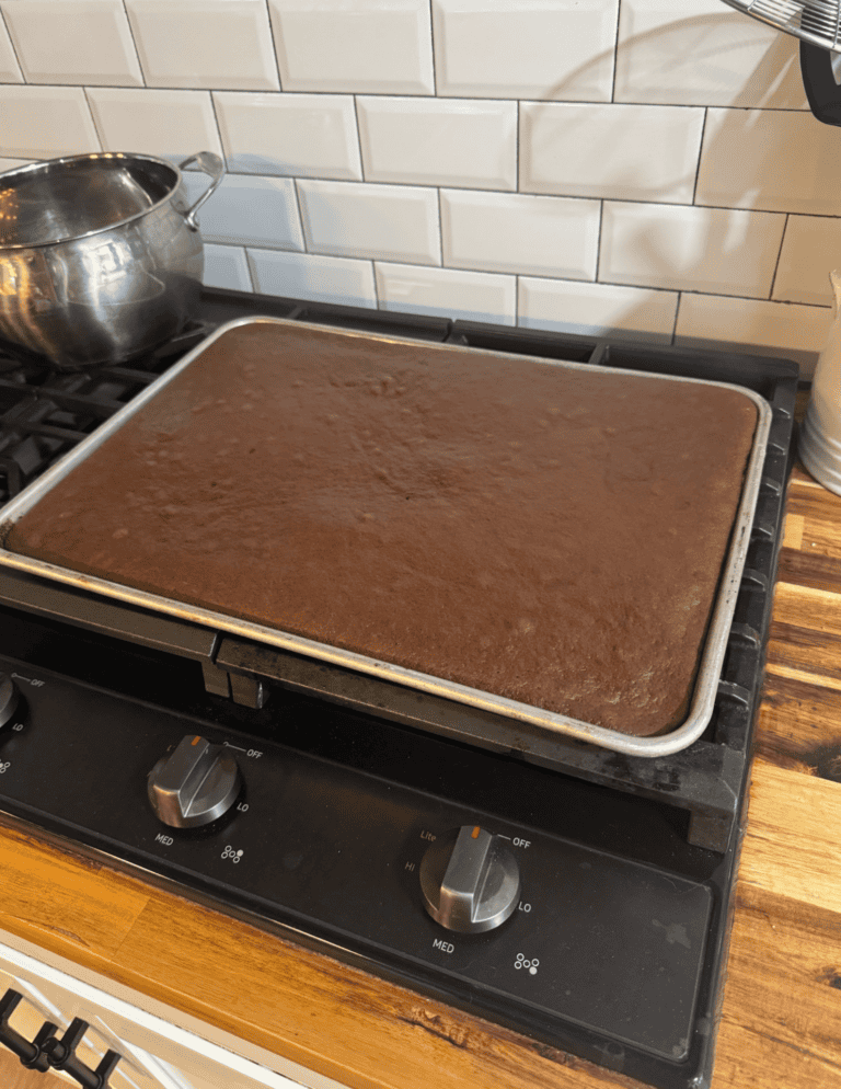 Freshly baked chocolate sheet cake cooling on a stovetop.