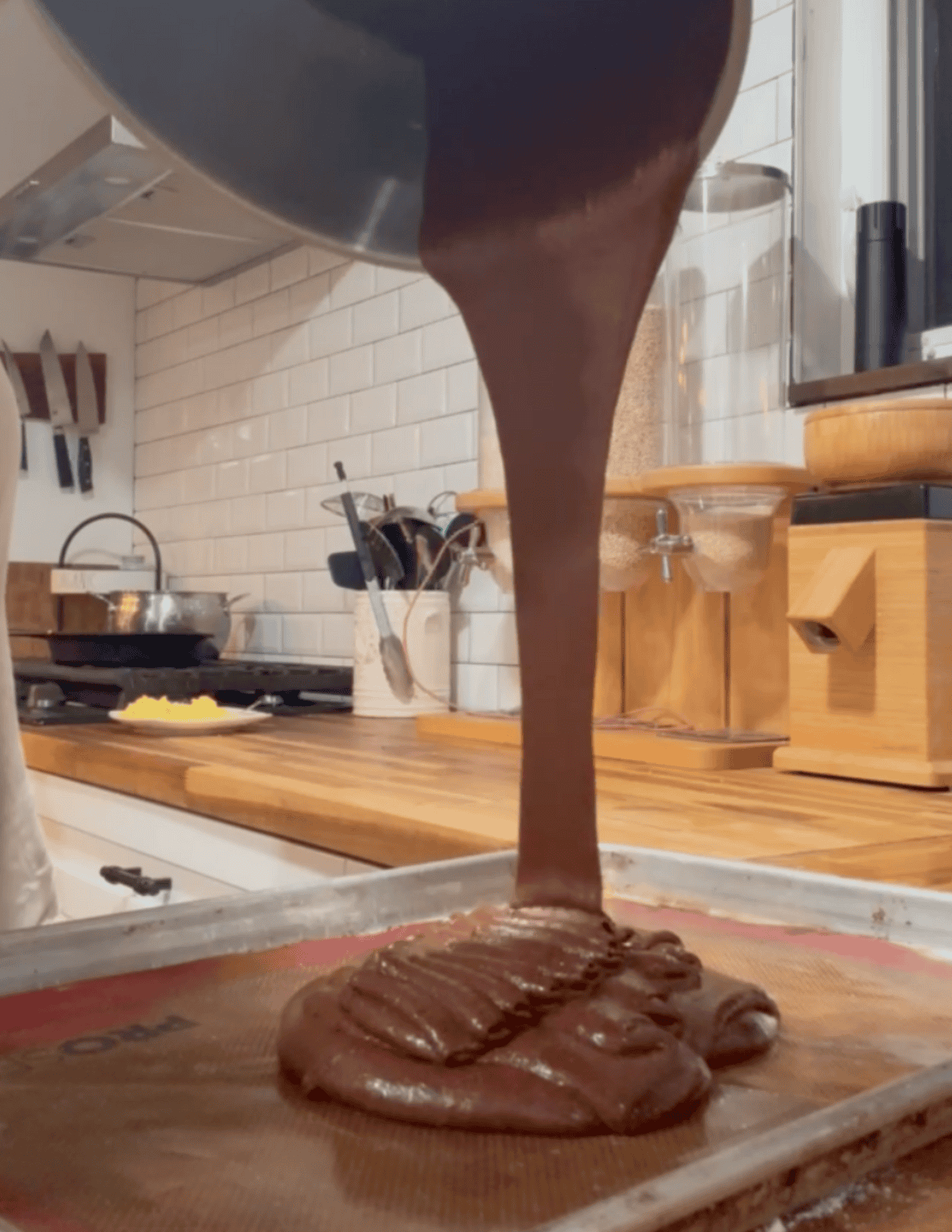 Delicious homemade chocolate fudge being poured onto a tray in a cozy kitchen.