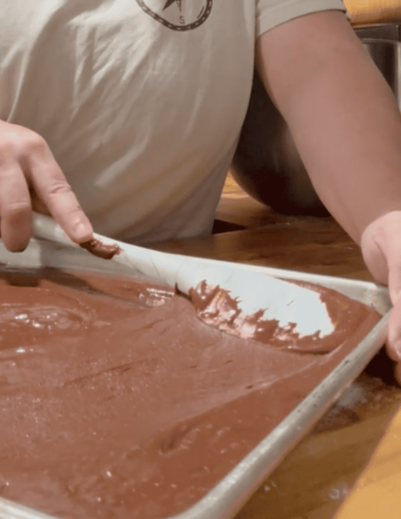 Person spreading chocolate batter in a baking tray for homemade treats.