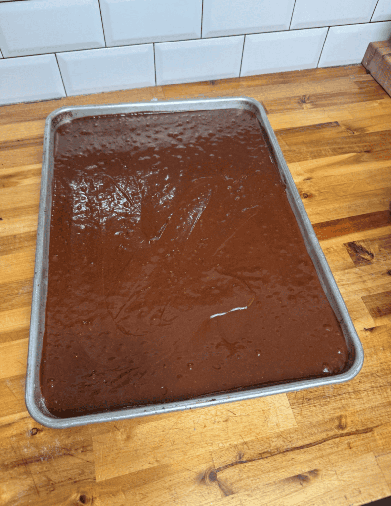 Freshly made chocolate fudge on a baking sheet in a kitchen setting.